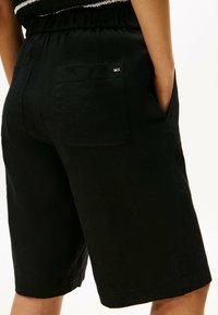Shorts neri in lino con vita elastica, dotati di due tasche posteriori e un piccolo logo decorativo. Il tessuto ha una texture liscia.
