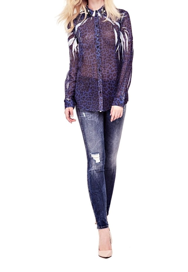 Sheer purple blouse with white floral patterns, paired with blue ripped skinny jeans. Model wearing beige heels, standing against a white background.