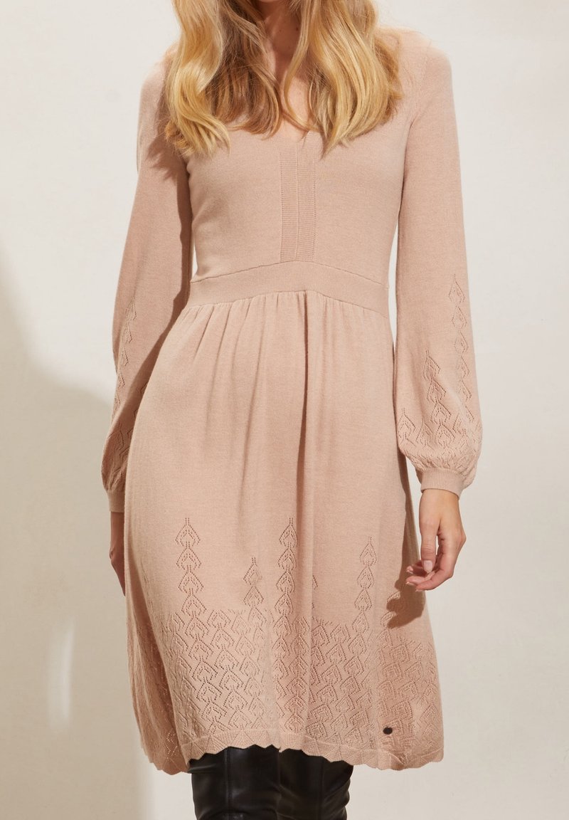 Stickad klänning i mjuk rosaton med långa, puffiga ärmar, en plisserad kjol och intrikata bladmönster broderade längs nederkanten.