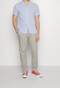 Ljusblå kortärmad skjorta, knäppt, med krage. Beiga linneblandade byxor. Röda sneakers med vita sulor och snörningar. Avslappnad outfit.