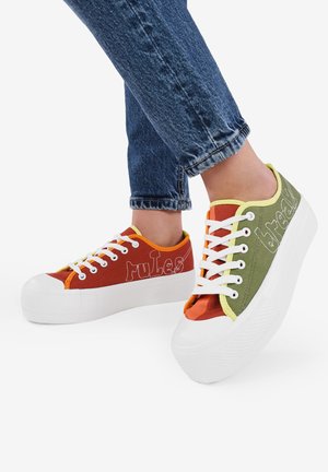 Zapatillas de lona multicolores con suela de goma blanca, parte delantera con cordones y texto bordado en paneles contrastantes.
