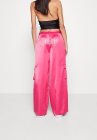 Rosa satinkargo-byxor med större fickor, med en "Juicy"-logotyp i rhinestones på baksidan. Lös passform med en slät textur.