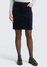 Marineblaue Cord-Rock mit Fronttaschen, Knopfverschluss, knielangem Design, kombiniert mit schwarzen Slippers und transparenten schwarzen Strumpfhosen.