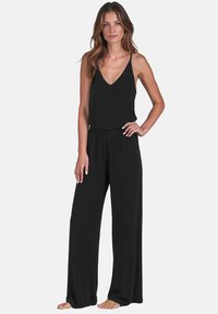 Sort, ærmeløs jumpsuit med V-udskæring og elastisk talje. Stoffet virker glat og let, og har brede, svævende ben.