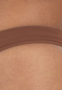 Bruine elastiek rustend tegen een gladde, tan huidoppervlak, laat een naadloze textuur en zacht, rekbaar materiaal zien.