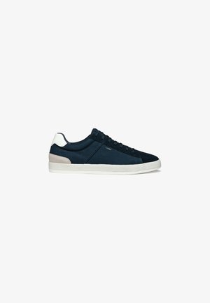 Baskets en toile bleu marine avec une finition texturée, présentant une semelle blanche et des accents beige sur le talon, un design à lacets, avec un branding minimal.
