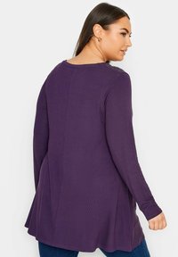 Lila långärmad topp med en utsvängd nederkant, med rundad halsringning och subtila texturerade accenter längs ryggen. Tillverkad av mjukt tyg.