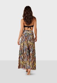 Musta bandeau-bikinitoppi, jossa on solmittava selkäpuoli, yhdistettynä ilmavaan, moniväriseen hameeseen, jossa on elävä abstrakti kuvio ja kevyttä kangasta.