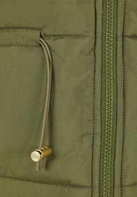 Maslinasto zelena, podstavljena jakna s vertikalnim patentnim zatvaračem i vrstom za stezanje s zlatnom metalnom čepom i džepom.