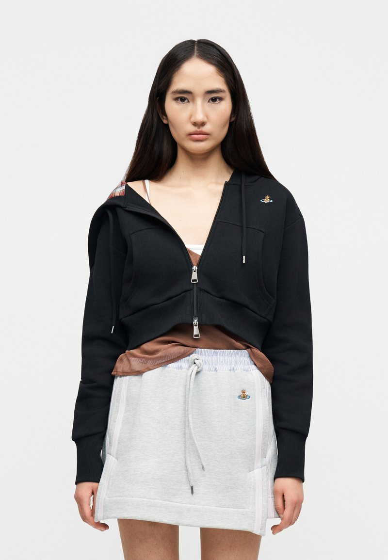 Hoodie noir court avec fermeture éclair à l'avant, doublé d'un tissu à carreaux, associé à une jupe sweat grise avec cordon de serrage et détails brodés.