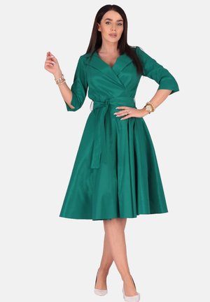 Grünes, knielanges Kleid aus Satinstoff. Wickeldesign mit großem Kragen, Dreiviertelärmeln und passendem Gürtel. Ausgestellter Rock mit Falten.