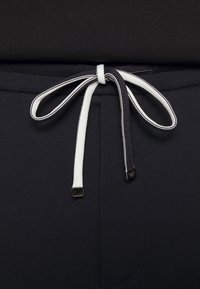 Czarny rozciągliwy pas z kontrastowym czarno-białym sznurkiem, charakteryzujący się gładką teksturą i eleganckim designem. Widoczne małe detale metalowe.