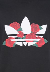 Fekete póló fehér Adidas logóval, három csíkkal, valamint vörös és zöld virágos rózsa grafikákkal a logó körül.