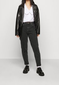 Svart konstläder blazer, vit skjorta med rynkad krage, mörkgrå högmidjade jeans och svarta kraftiga snörskor.