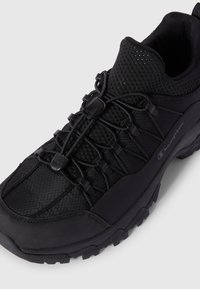 Schwarzer Outdoor-Schuh mit Mesh-Obermaterial, verstärkter Zehenkappe, elastischem Schnürsystem und strukturiertem Sohlenprofil. Leichtgewichtig mit Dämpfungselementen.