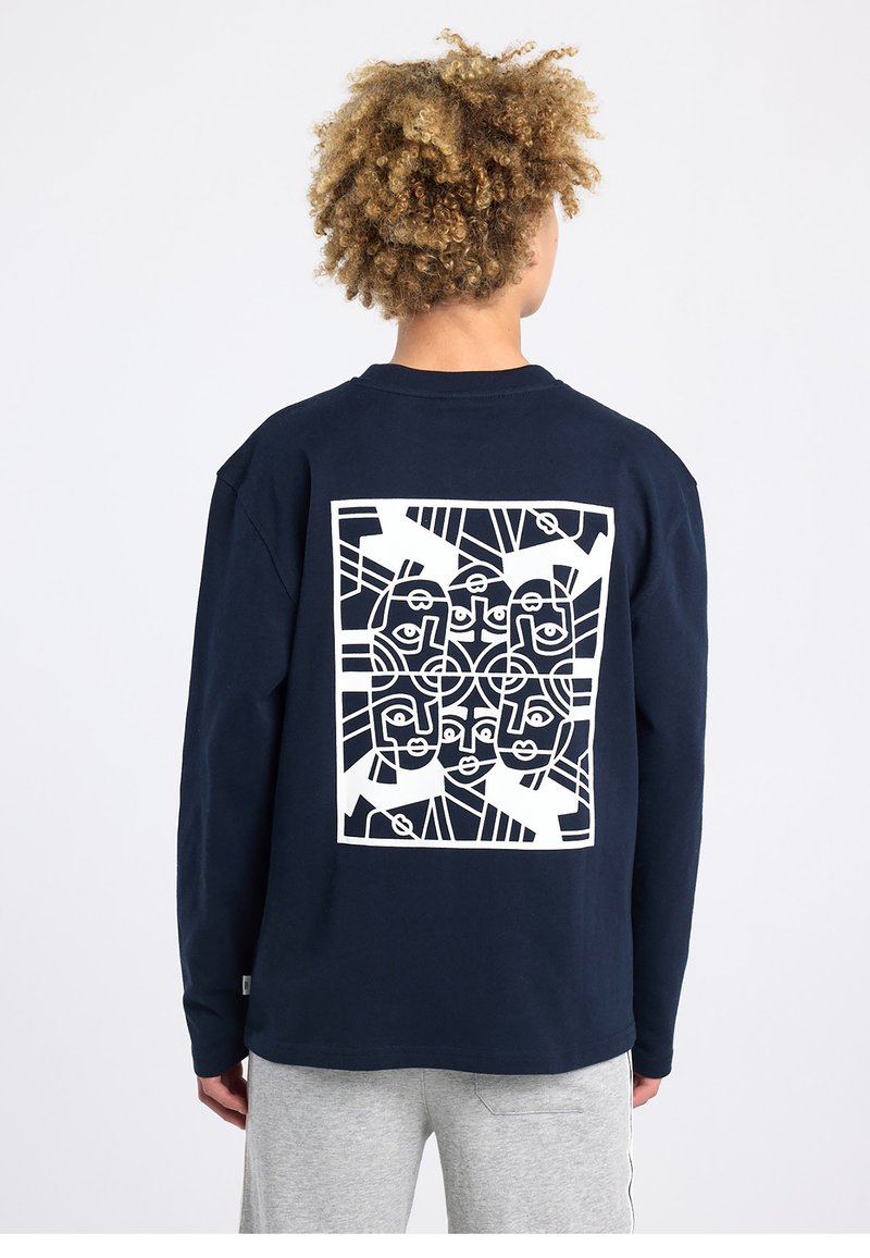 T-shirt à manches longues bleu marine avec un motif géométrique blanc représentant un visage au dos. Col rond, tissu doux et coupe décontractée.