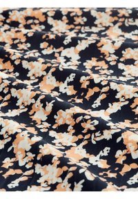 Le tissu floral présente un fond bleu marine avec des fleurs orange et blanches. Surface texturée, légère et drapée avec douceur.