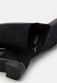 Stivale alla caviglia nero realizzato in materiale liscio con punta rotonda, cerniera discreta e suola in gomma testurizzata. La fodera interna è morbida e scura.