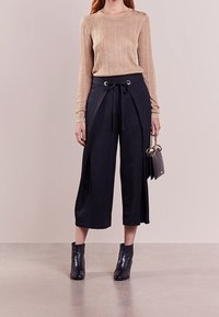 Top de mangas largas acanalado dorado, pantalones negros de pierna ancha con cinturón anudado, botines negros y un pequeño bolso negro. Materiales suaves y texturizados.