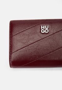 Burgundy leather wallet with diagonal stitching, embossed "HUGO" logo in silver, and a smooth texture. Compact rectangular shape.