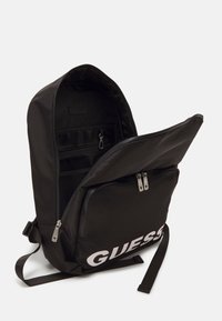 Zwarte rugzak met een gladde, matte afwerking. Bevat een hoofdcompartiment met een ritssluiting en een voorzak. Opvallend merkteken weergegeven.