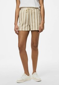 Shorts rayés beiges avec taille élastique et cordon de serrage, fabriqués à partir d'un tissu doux, dans une coupe décontractée. Portés avec des baskets blanches.