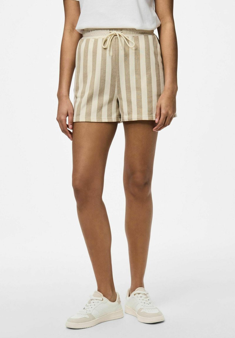 Shorts rayés beiges avec taille élastique et cordon de serrage, fabriqués à partir d'un tissu doux, dans une coupe décontractée. Portés avec des baskets blanches.