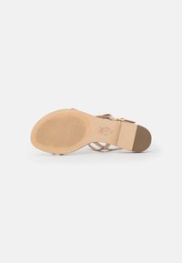 Sandalo con tacco alto beige con suola testurizzata, design aperto sulla punta e cinturini sottili. Sottotoni dorati vicino alla caviglia.