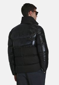 Zwarte pufferjack met een glanzende bovenkant en een matte onderkant. Voorzien van een hoge kraag en een gestikt ontwerp.
