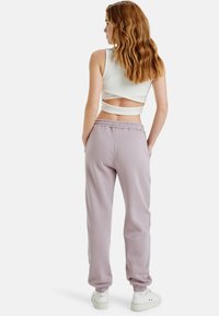Lichtpaarse sweatpants met elastische tailleband, voorzien van twee zijzakken. Gekozen in combinatie met een witte cropped tanktop met een uitsnede op de rug.