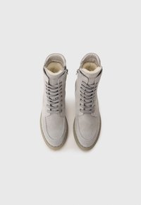 Graue Wildleder-Stiefeletten mit Schnürung, Reißverschluss und weicher Innenauskleidung. Abgerundete Zehenpartie und eine flache, strukturierte Sohle.