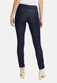 Jeans skinny in denim blu scuro, con vita alta, due tasche posteriori e dettagli di cucitura. Abbinati a stivaletti beige fino alla caviglia.