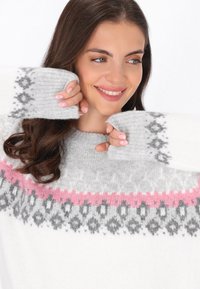 Suéter de punto blanco con patrones geométricos en gris y rosa, con un escote amplio y puños de canalé. Textura suave y diseño cálido.