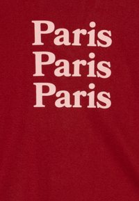 T-shirt en coton rouge avec "Paris" imprimé trois fois en typographie blanche, en gras, sans-serif, centré sur le devant.