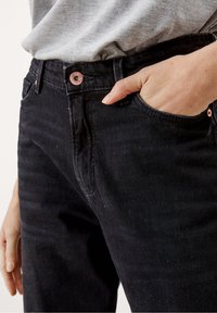 Czarne jeansy z denimu o dopasowanym kroju, widocznymi przednimi kieszeniami i guzikiem w kolorze różowego złota. Materiał ma subtelną fakturę i delikatne przetarcia.