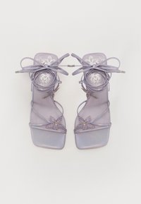 Sandales à talons lavande avec des fines lanières, des embellissements floraux, une finition irisée et un design à bout carré. Liens en dentelle à la cheville.
