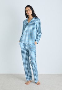 Conjunto de pijama em padrão pied-de-poule azul e branco, composto por uma camisa de botão de mangas compridas e calças de perna reta, ambos feitos de um tecido suave com um padrão quadriculado.