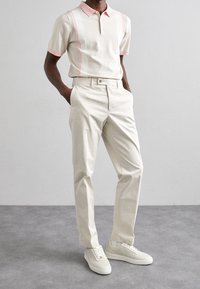 Ljusbeige polo med rosa accenter, korta ärmar och ribbat mönster, tillsammans med krämfärgade byxor och vita sneakers.