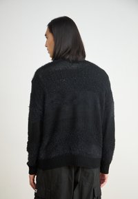 Black knitted sweater featuring a textured design with varying patterns. Long sleeves and ribbed cuffs complete the relaxed fit.
