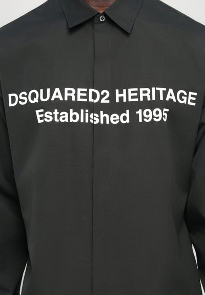 Mustasärk, millel on kraega disain ja mille esiküljel on suurelt valge tekst "DSQUARED2 HERITAGE Established 1995". Sile tekstuur.