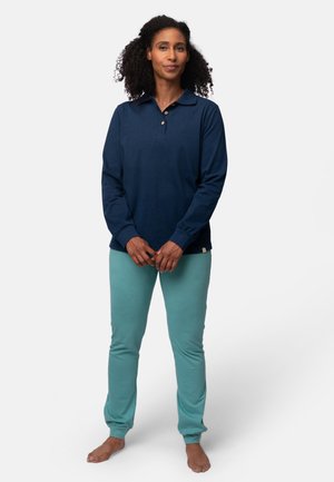 Marineblauwe polo met lange mouwen en een knoopsluiting op de kraag, gecombineerd met lichtteal ankle-lange broeken. De stof lijkt zacht en lichtgewicht.