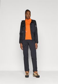 Melnā ūdensnecaurlaidīgā jaka, oranža vidējā slāņa veste, tumši bikses un brūni pastaigu zābaki ar oranžām šņorēm. Apģērbam ir rāvējslēdzēji un logotipi.