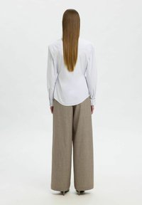 Camicia bianca a righe con maniche lunghe, abbinata a pantaloni ampi beige; tessuto morbido, vestibilità su misura e design minimalista.
