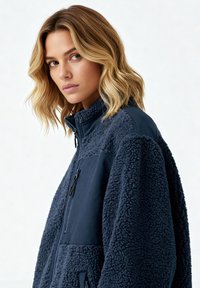 Veste en polaire bleu marine avec une finition texturée et duveteuse. Comprend un panneau avant en nylon lisse et une poche poitrine zippée. Conception à col montant.