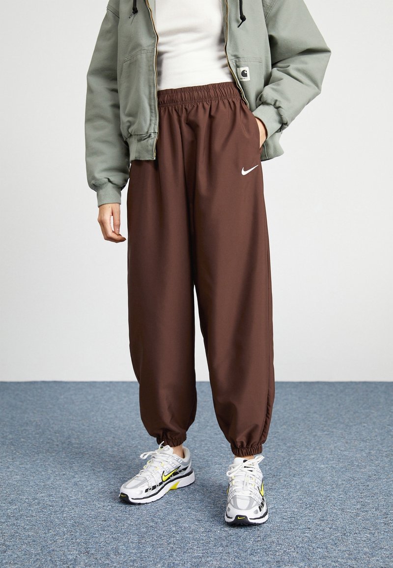Hnědé volné kalhoty s elastickým pasem a ohrnutými kotníky. V kombinaci se světle zelenou bundou a bílými teniskami Nike s akcenty.