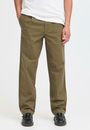 Olive green chinos made of cotton with a straight leg design. Features pockets and subtle stitching details. Worn with black shoes.