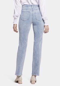 Jeans de denim de color azul claro con un diseño de pierna recta, cintura alta y dos bolsillos traseros. La tela presenta una textura deslavada y se combina con tacones beige.