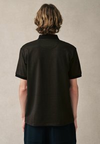 Polo noir à manches courtes avec un motif texturé, présentant un col et des accents noirs sur les manches et l'ourlet.