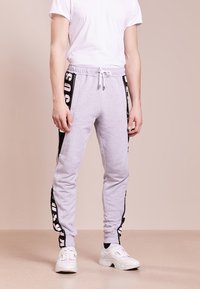 Grå joggingbyxor i mjukt tyg, med en svart sidostripe med vit text, elastisk midja med dragsko och åtsittande ribbade anklar.