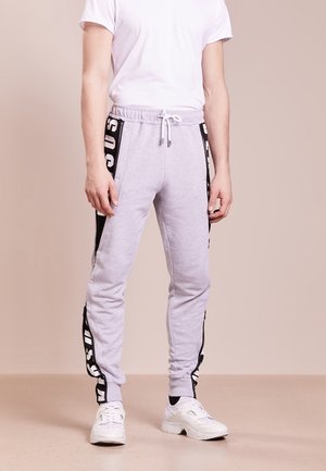 Graue Jogginghose aus weichem Material, mit einem schwarzen Seitenstreifen und weißem Text, elastischem Bund mit Kordelzug und eng anliegenden Bündchen an den Knöcheln.